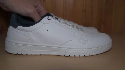 Side view 4K footage of putting brand new white sneakers on yellow wooden shelf Stock Footage 310130808