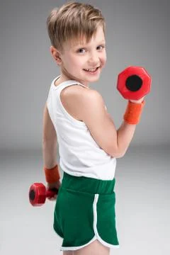 Side view of active boy training with dumbbells isolated on grey Stock Photos