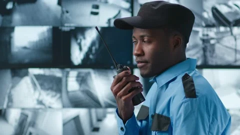 Side view of African-American security guard talk on radio in control room Stock Footage 180439695
