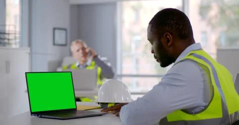 Side view of afro engineer in reflective vest looking at laptop screen in office Stock Photos