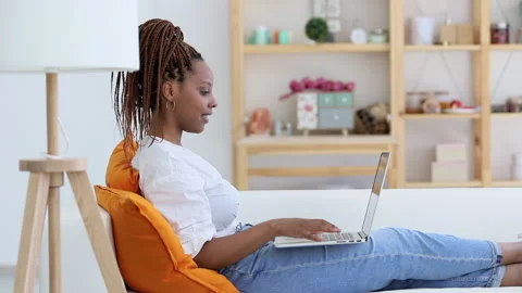Side view afro woman do video call on laptop in living room Spbi. modern Stock Footage 137559390