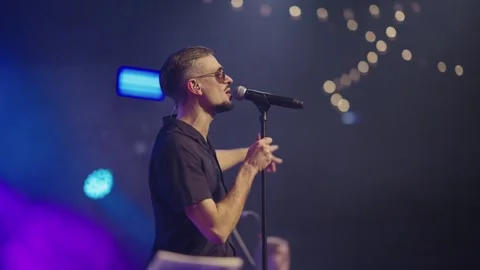 Side view artist in dark round glasses performs on club stage with band Stock Footage 244489962