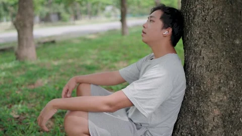Side view of Asian man leaning on a tree thinking outside sitting on floor Video stock 283187202
