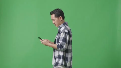 Side View Of Asian Man Using Mobile Phone While Walking On Green Screen Stock Footage 248007730