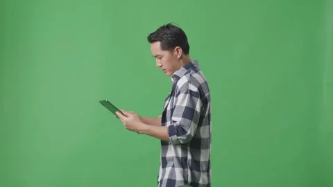 Side View Of Asian Man Using Tablet While Walking On Green Screen In The Studio Stock Footage 248007825