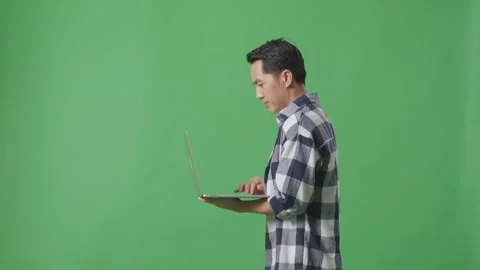 Side View Of Asian Man Using Laptop Computer While Walking On The Green Screen Stock Footage 248007902