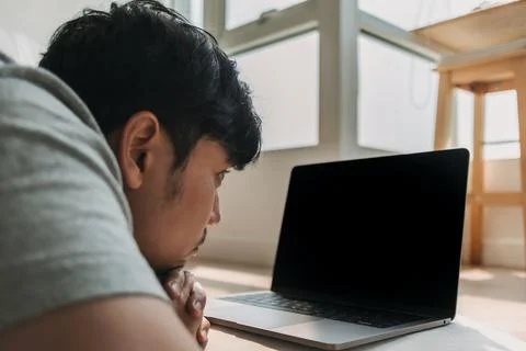 Side view of asian man using computer, lying on floor while working on laptop Foto stock