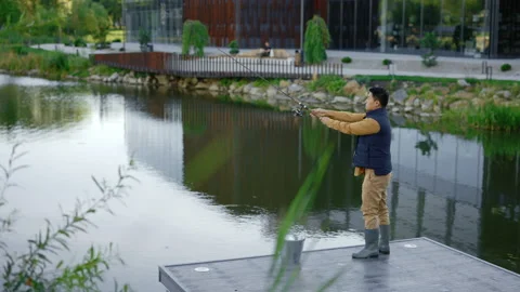 Side view of the asian man wearing waistcoat and fishing from the pier on the Stock Footage 227521550