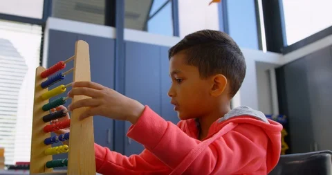 Side view of Asian schoolboy solving math problem with abacus at desk in a Stock Footage 106934948