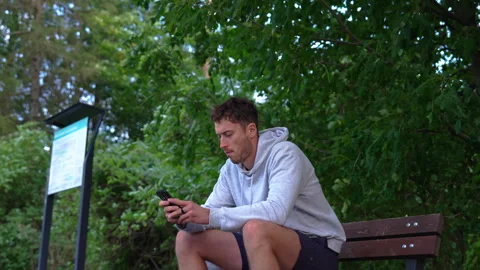 Side View of Athlete Using Phone on Park Bench 스톡 동영상 347811595
