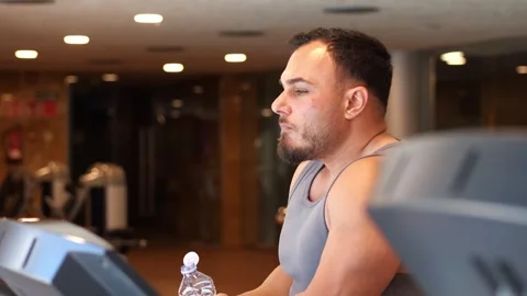 Side view of an athletic man drinking water from a plastic bottle during a .. Vidéo 344049093