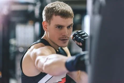 Side view of athletic man punching a bag with kickboxing gloves in the gym wo Stock Photos