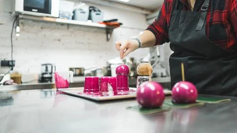 Side view of a baker decorating chocolate balls with pink cream in the bakery Stock Photos