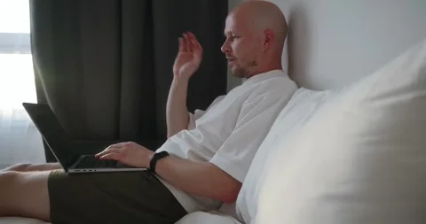 Side view, a bald male freelancer communicates via video call using his laptop Stock Footage 302901310