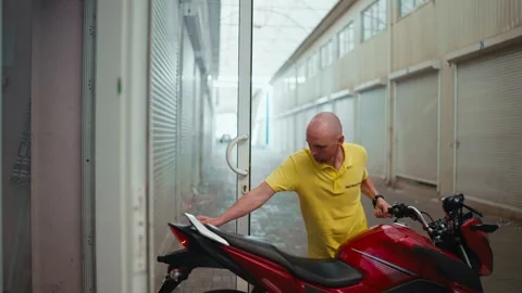Side view. A bald man driving instructor in a yellow T-shirt drives a red moped Stock Footage 249606160