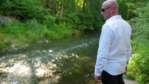 Side view of a bald man looking at the current river, under the bridge. Medium Stock Footage 115026372