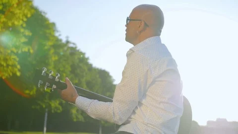 Side view of a bald man plays guitar and sings in park. Guitarist touching Stock Footage 112828759