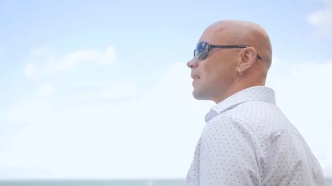 Side view of bald man standing on the beach. He is looking at sea. Close up shot Stock Footage 113274702