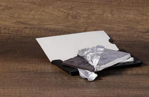 Side view of a bar of dark chocolate in an open package. Stock Photos