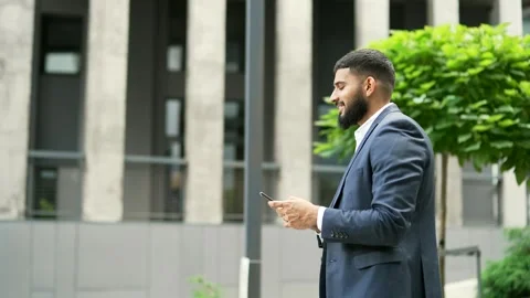Side view of bearded businessman in formal suit looking at mobile phone walking  Stock Footage 265032409