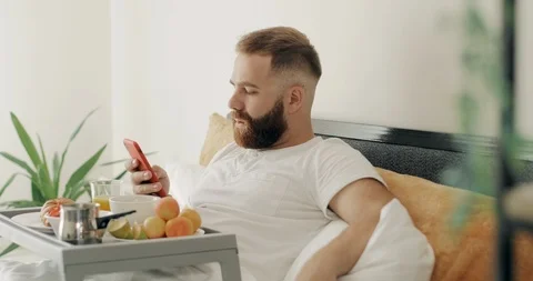 Side view of bearded guy typing message on his smartphone while sitting with Video stock 127351249