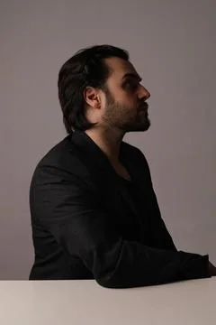 Side-view of bearded man in black suit sitting over white background. Vertical. Stock-Fotos