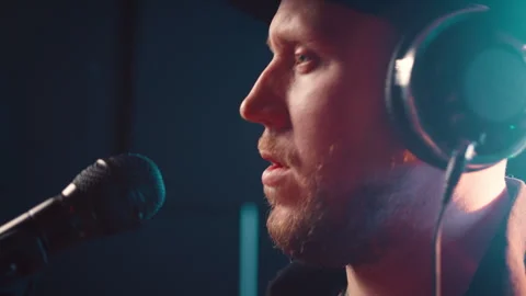 Side view bearded man in cap and headphones records music in studio, while Stock Footage 274150940