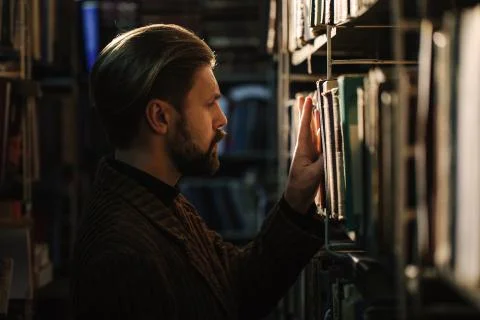 Side view of bearded man choosing book at public library Stock Photos