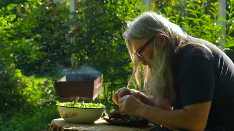 Side View of Bearded Man Eating Grilled Fish with Hands in Garden Stock Footage 328361688
