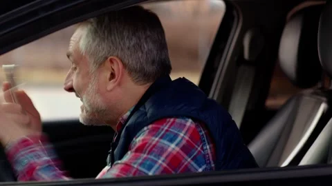 Side view of a bearded man sitting in a car with a phone. A gray-haired man Stock Footage 242610721