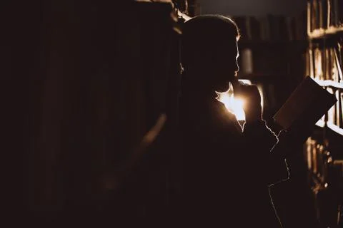 Side view of bearded reader standing with book at library Stock Photos
