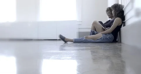 Side view of beautiful dark young women sat on floor in empty room 4K Stock Footage 78832695