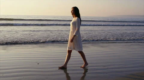 Side view of beautiful woman walking on wet sea shore at sunset Stock Footage 59057135