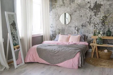 Side view on a bed with grey and pink bedding, white mirror and vases with fl Stock Photos