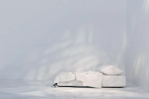 Side view of bed with white linen. Light and shadows on white wall Stock Photos