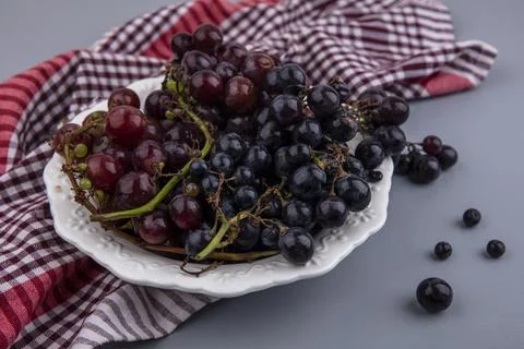 Side view of black and red grapes in plate on plaid cloth and gray background Stock Photos