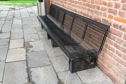 Side view of a black bench made of metal rods on a paved gray stone sidewalk Stock Photos