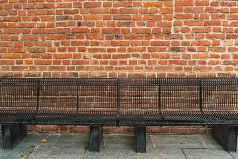 Side view of a black bench made of metal rods on a paved gray stone sidewalk Stock Photos
