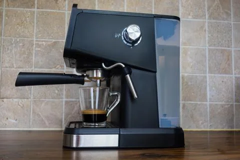 Side view of black espresso machine brewing coffee into glass mug on table Stock Photos