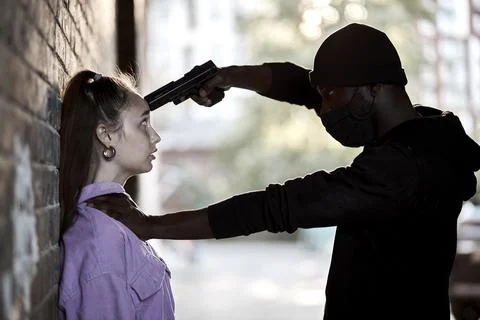 Side view black man use gun to intimidate caucasian woman for rape. Female is Stock Photos