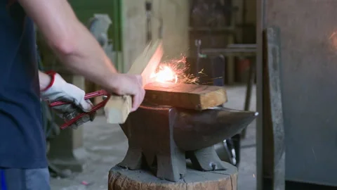 Side View of Blacksmith Hammering Hot Metal with Wood on Anvil Stock Footage 313850029