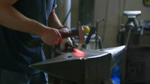 Side View of Blacksmith Hammering Hot Metal – Forge Glow in Foreground Stock Footage 313864589