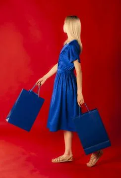 Side view of blond model in blue dress with shopping bags no face visible is Stock Photos