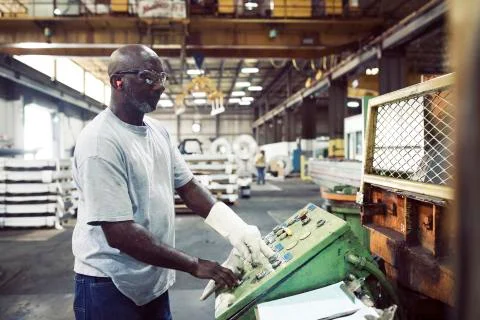Side view of blue collar worker using control machine while working in steel Fotos de archivo