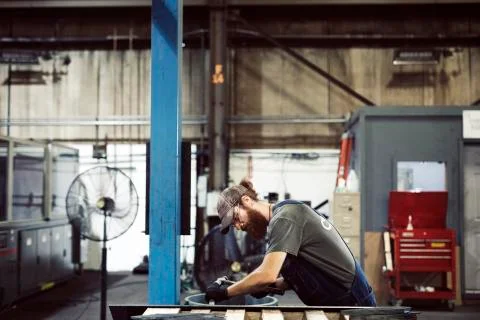 Side view of blue collar worker using hammer and chisel in steel factory Fotos de archivo