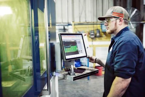 Side view of blue collar worker using desktop computer while working in steel Fotos de archivo