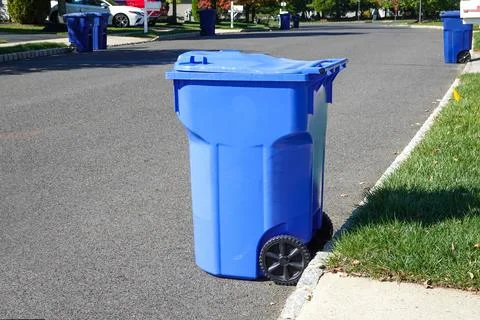 Side view of a blue recycling bin on an asphalt street near a curb Stock Photos