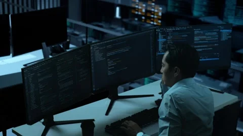 Side View Of Bored Asian Man Write Code With Multiple Computer Screens In office Stock Footage 255846609