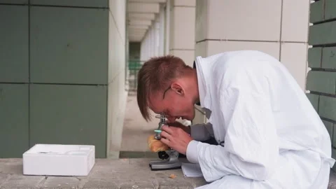 Side View of Botany Student in White Coat Examining Pastry Through Microscope 스톡 동영상 321115470