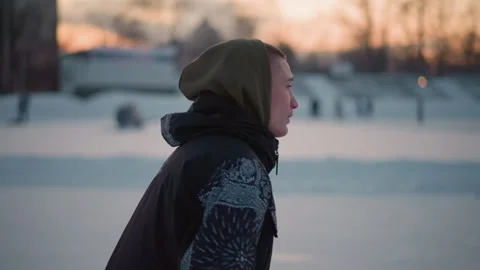 Side view boy gliding smoothly on ice ring wearing winter jacket at sunset Stock Footage 316457535